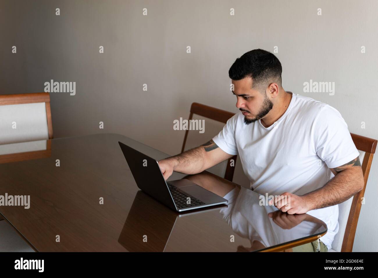 Latino homme avec des tatouages qui fingerent un écran d'ordinateur portable avec un visage sérieux Banque D'Images