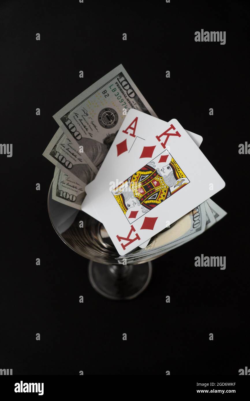 Cartes de poker Roi As de diamant haute carte avec 300 billets de dollar sur fond noir verre cocktail Banque D'Images