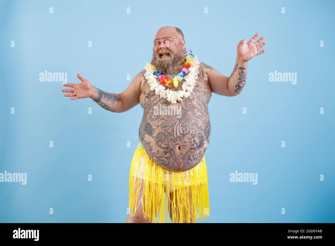 Positif homme gras avec tatouages dans la jupe décorative herbe danse sur fond bleu clair Banque D'Images