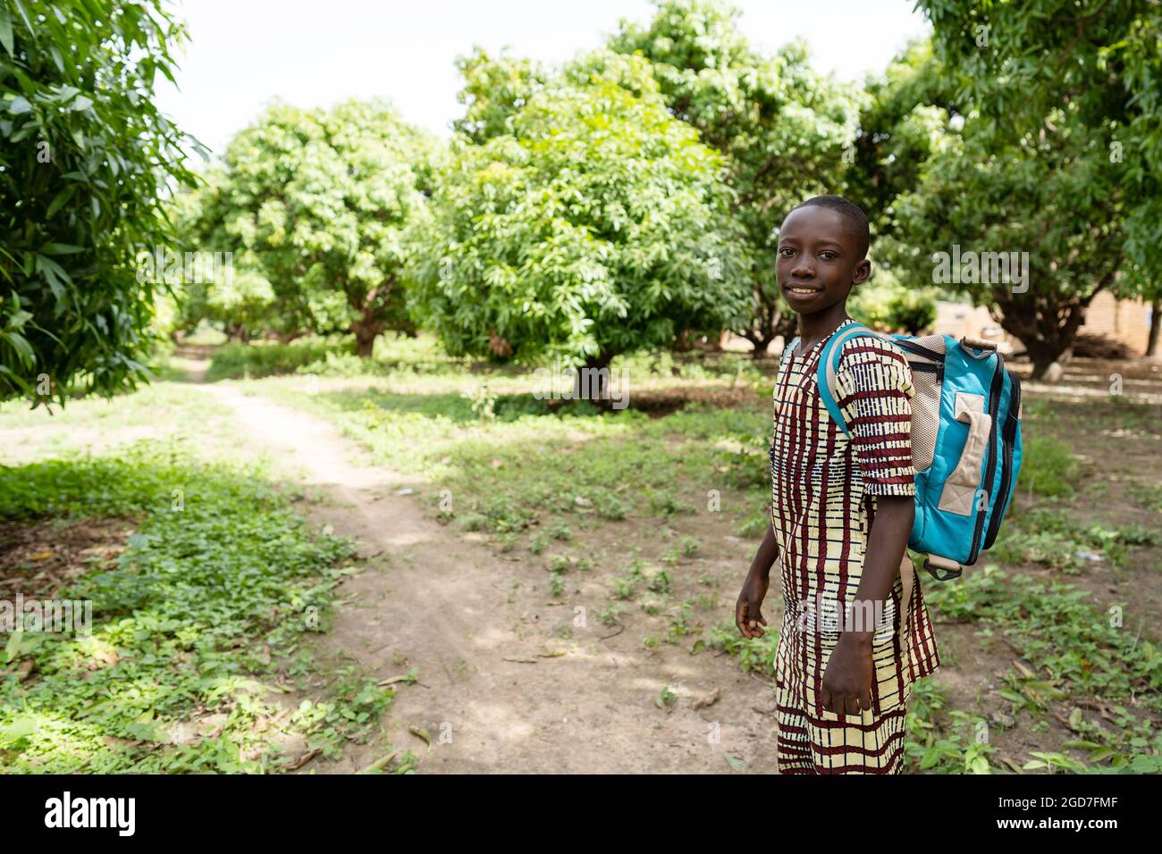 Bon petit écolier africain sur le chemin de l'école marchant sur un petit chemin de terre au milieu d'une forêt de mangues Banque D'Images