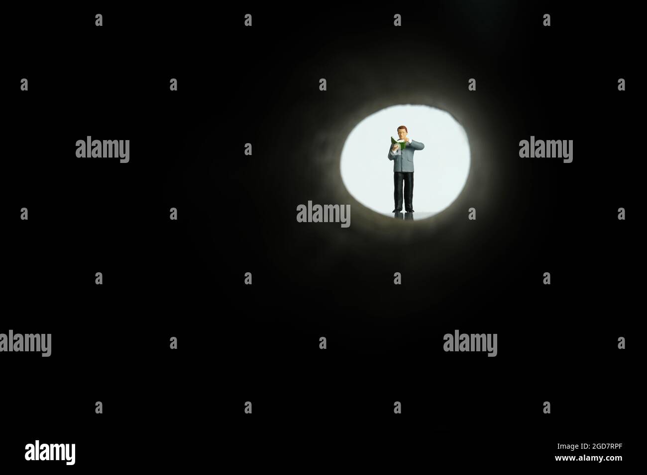 Photographie miniature de personnage de jouet de personnes. Un homme à la recherche d'un indice, d'un conseil, d'un guide, sur une allée sombre tout en lisant un livre. Photo d'image Banque D'Images