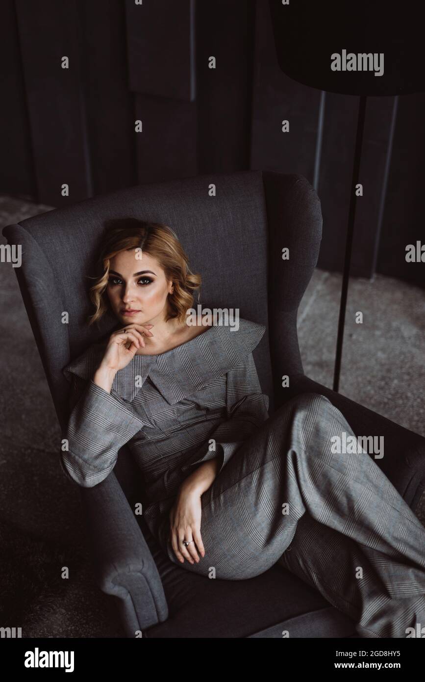 Belle jeune femme d'affaires dans un élégant costume gris assis sur une chaise dans un bureau avec un intérieur moderne, regardant la caméra. Portrait d'un char Banque D'Images