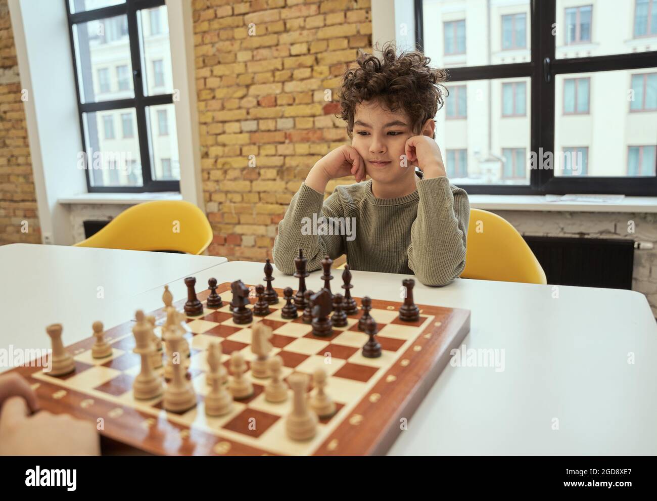 Observant petit garçon assis dans la salle de classe et jouant aux échecs sur l'échiquier Banque D'Images