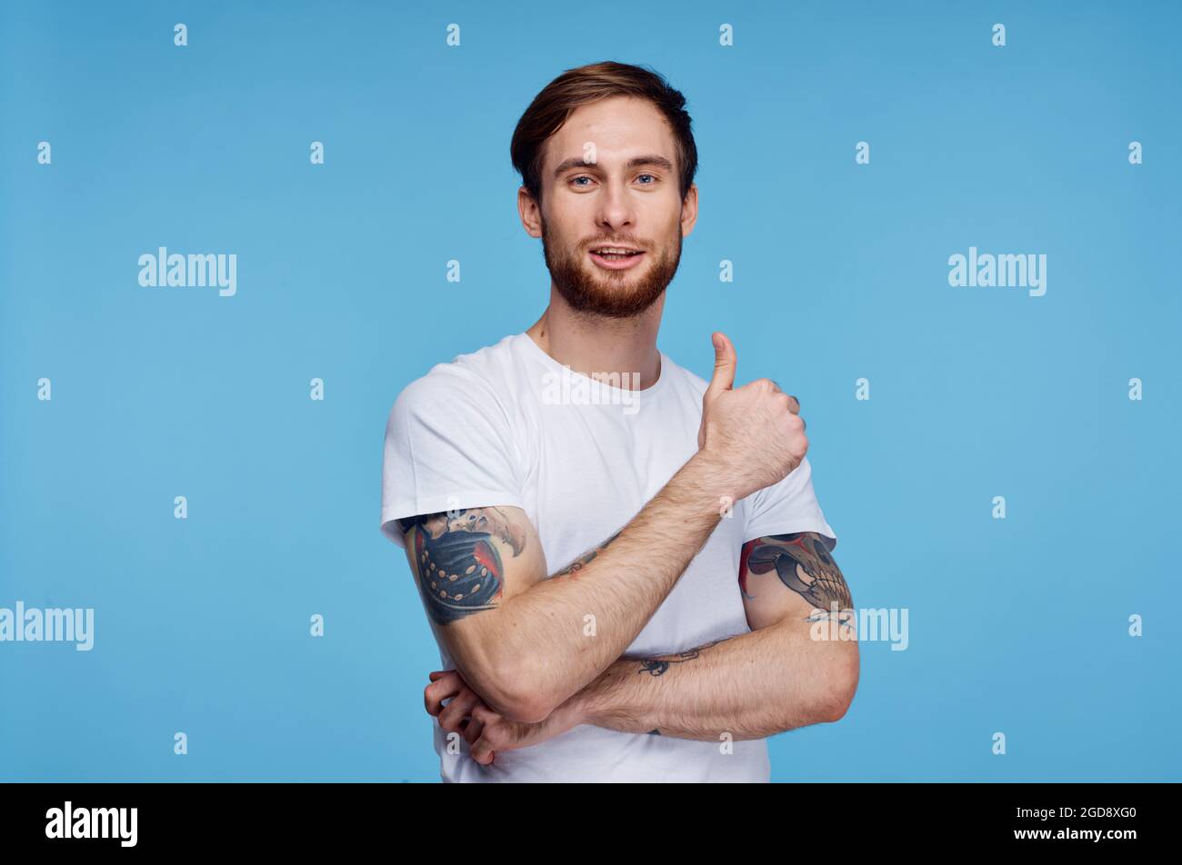 homme joyeux avec des tatouages sur les bras dans un t-shirt blanc sur fond bleu Banque D'Images