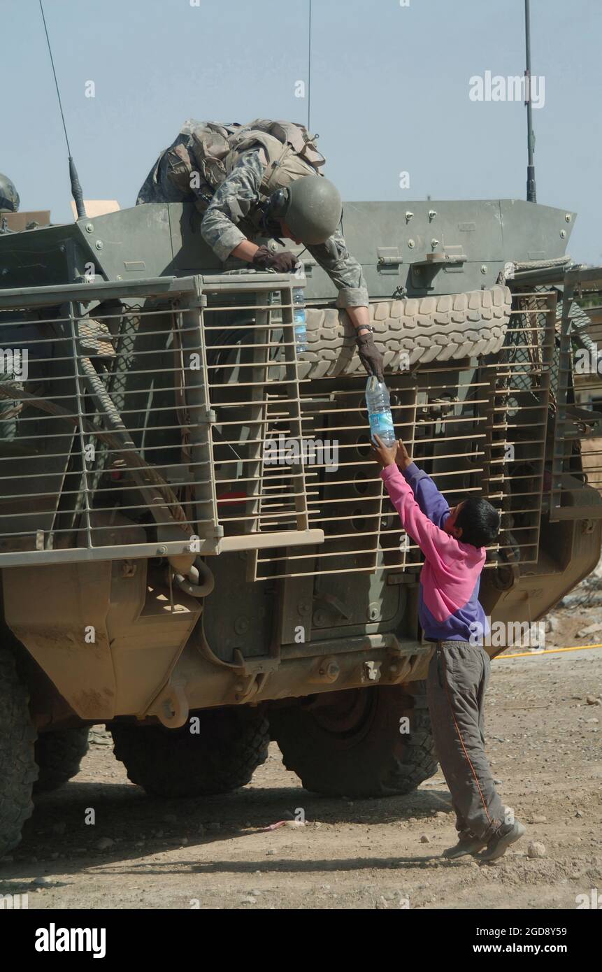 Un soldat de l'armée américaine (États-Unis) de la 172e équipe de combat de la Brigade Stryker, fort Wainwright, Alaska (AK), à bord d'un véhicule porteur d'infanterie Stryker M1126, remet une bouteille d'eau à Mosul, en Irak, pendant l'opération LIBERTÉ IRAQUIENNE. Le Stryker est équipé d'une cage de protection Slat Armor. (PHOTO USAF PAR SSGT JAMES L. HARPER JR. 051010-F-4177H-063) Banque D'Images