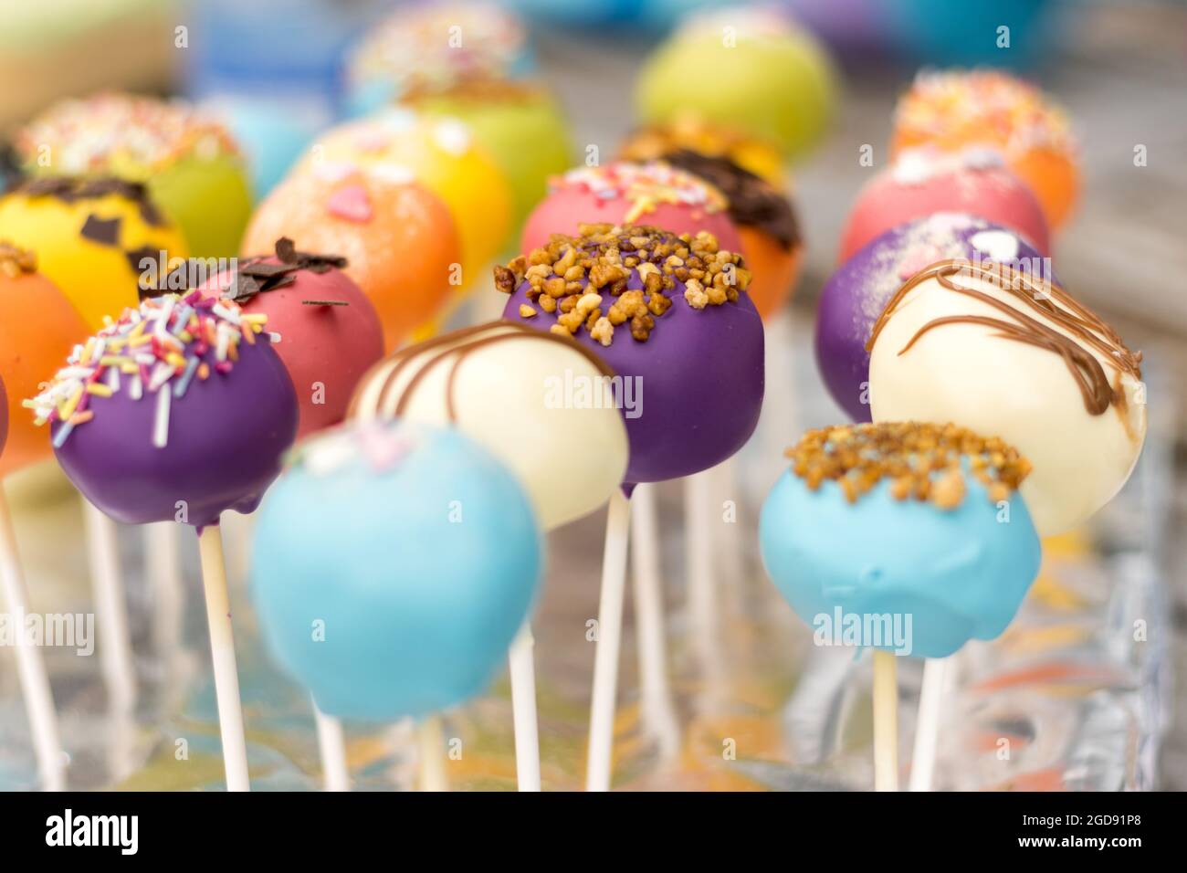 Un assortiment coloré de gâteaux pop, magnifiquement décorés avec des pépites, du filet de chocolat et des revêtements vibrants, affichés sur des bâtons. Banque D'Images