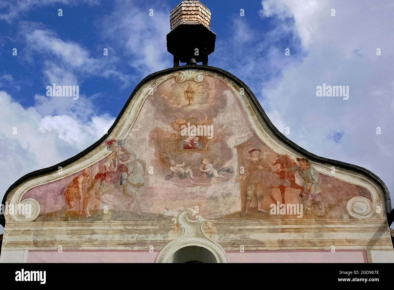 Des fresques décolorées attribuées au peintre de l'église Josef Anton Puellacher (1737-1799) décorent le pignon gracieux de l'Ortskapelle sur le bord de la route baroque ou la chapelle locale de Fronhausen sur le plateau Mieming ou Mieminger, une terrasse de montagne jusqu'à 1,000 m (3,280 pi) au-dessus de la vallée de l'auberge supérieure dans le Nord Tyrol, en Autriche. Les œuvres d'art, au-dessous d'un bellcote orné de bois, présentent Saint Martin de Tours qui divise son manteau avec un mendiant et deux hommes avec un cheval. Entre eux, il y a des anges volants et une Madonna et un enfant dans un cadre orné. Banque D'Images