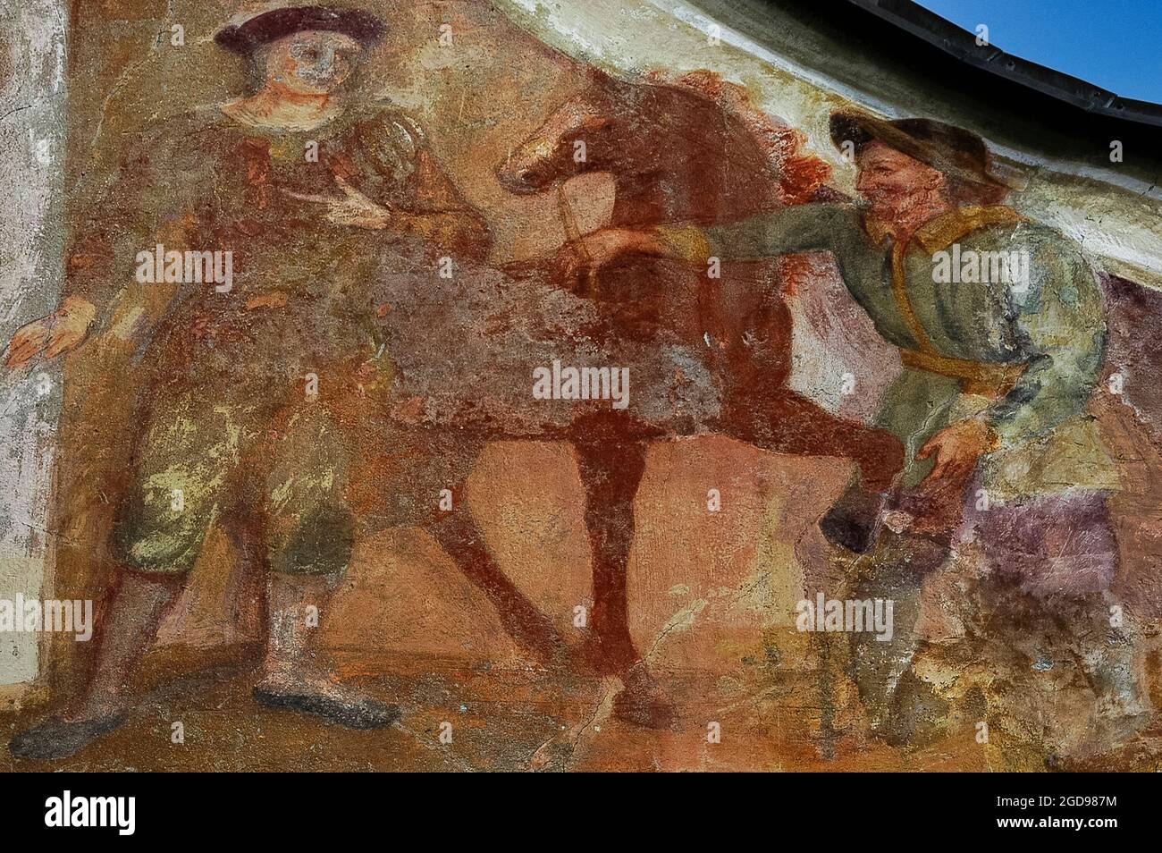 Des fresques décolorées attribuées au peintre de l'église Josef Anton Puellacher (1737-1799) décorent le pignon gracieux de l'Ortskapelle sur le bord de la route baroque ou la chapelle locale de Fronhausen sur le plateau Mieming ou Mieminger, une terrasse de montagne jusqu'à 1,000 m (3,280 pi) au-dessus de la vallée de l'auberge supérieure dans le Nord Tyrol, en Autriche. Les œuvres d'art, au-dessous d'un bellcote à bois, présentent ces deux hommes avec un cheval, et Saint Martin de Tours divisant son manteau avec un mendiant. Entre eux, il y a des anges volants et une Madonna et un enfant dans un cadre orné. Banque D'Images