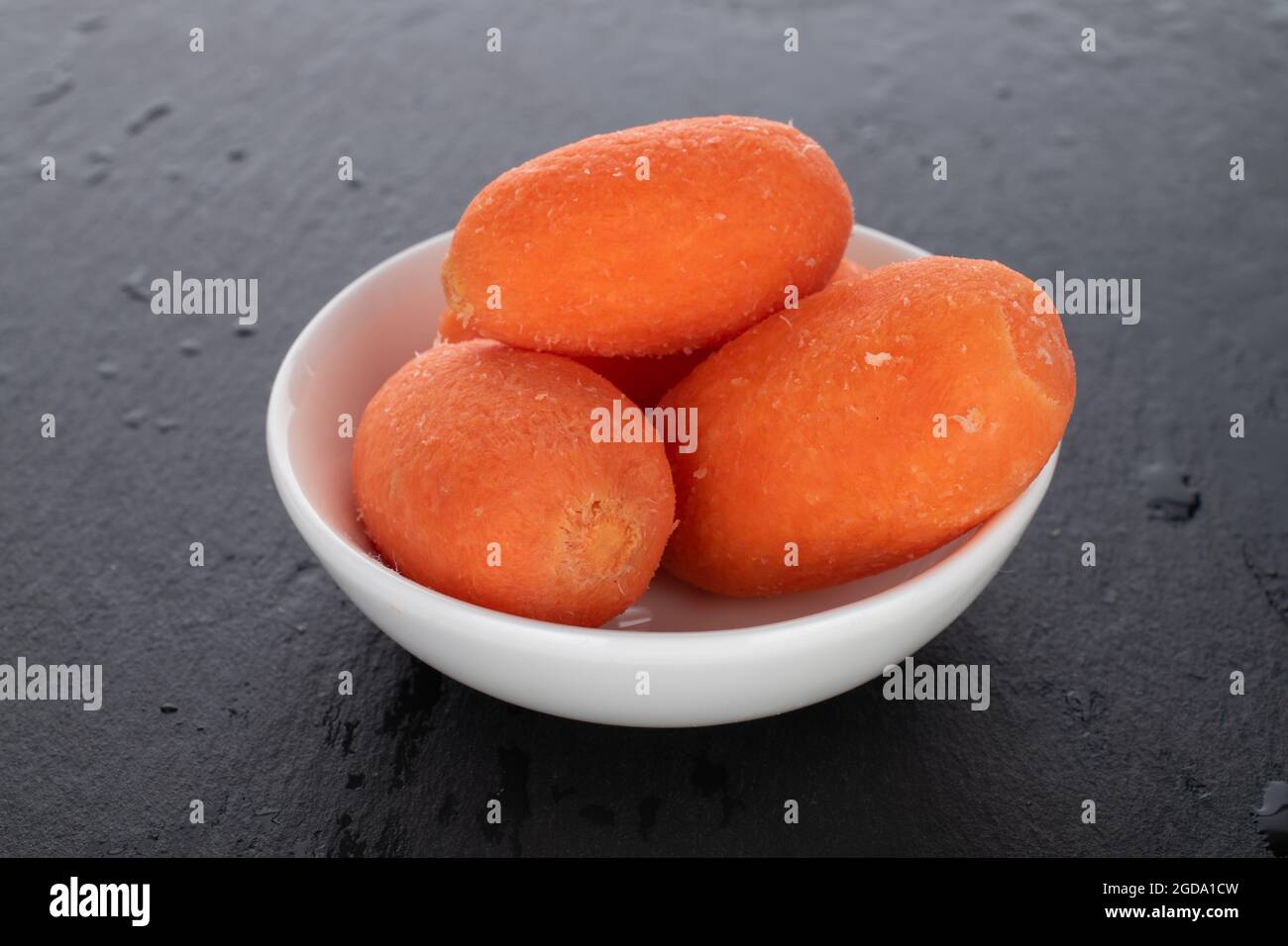 Plusieurs mini carottes, naturelles et juteuses d'orange vif dans un plat en céramique blanche, gros plan, sur une planche à servir en ardoise. Banque D'Images