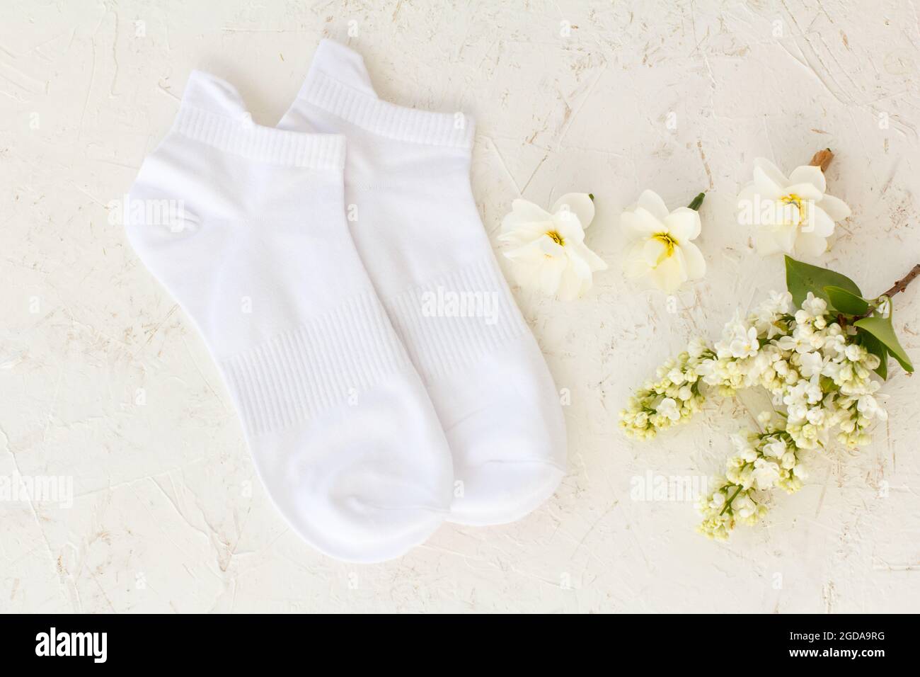 Paire de chaussettes blanches, fleurs de jasmin et bourgeons de fleurs de jonquilles sur fond blanc structuré, vue du dessus. Banque D'Images