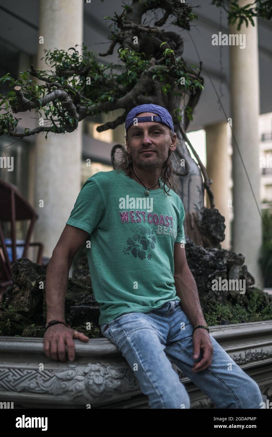 Homme mature en t-shirt, jeans et casquette assis dans la rue en ville. Cheveux longs gris. Photo de haute qualité Banque D'Images