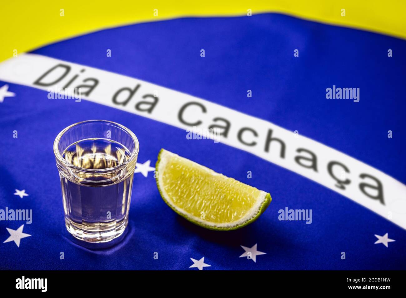 Coupe de cachaça ou de pinga brésilien, avec le drapeau brésilien en arrière-plan et texte en portugais: Cachaça Day Banque D'Images