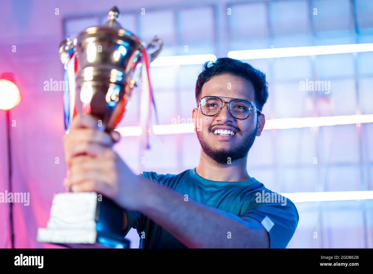 Joyeux gamer souriant avec des écouteurs célébrant en organisant le trophée gagnant sur la scène du tournoi de jeu esports Banque D'Images