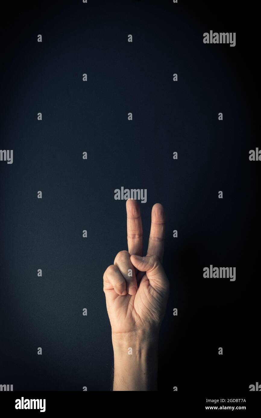 Image couleur dramatique de la main masculine démontrant le langage des signes numéro deux sur fond sombre avec espace de copie vide pour les éditeurs Banque D'Images