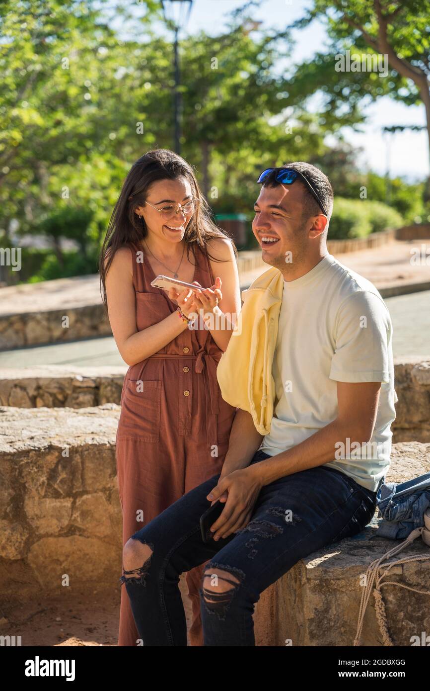 Deux amis souriant avec un téléphone portable à portée de main. Ils sont heureux dans un parc. Ils sont blancs. Ils rient ensemble. Javea, Alicante. Banque D'Images