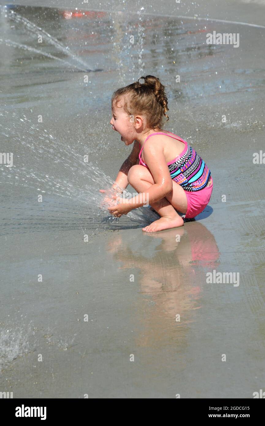 Un Bebe Qui Se Met A Genoux Par Dessus L Event De Pulverisation Du Parc Aquatique La Bouche Est Ouverte Et Les Yeux Fermes Comme Elle Exprime Son Plaisir Combinaison De Bain Rose Et