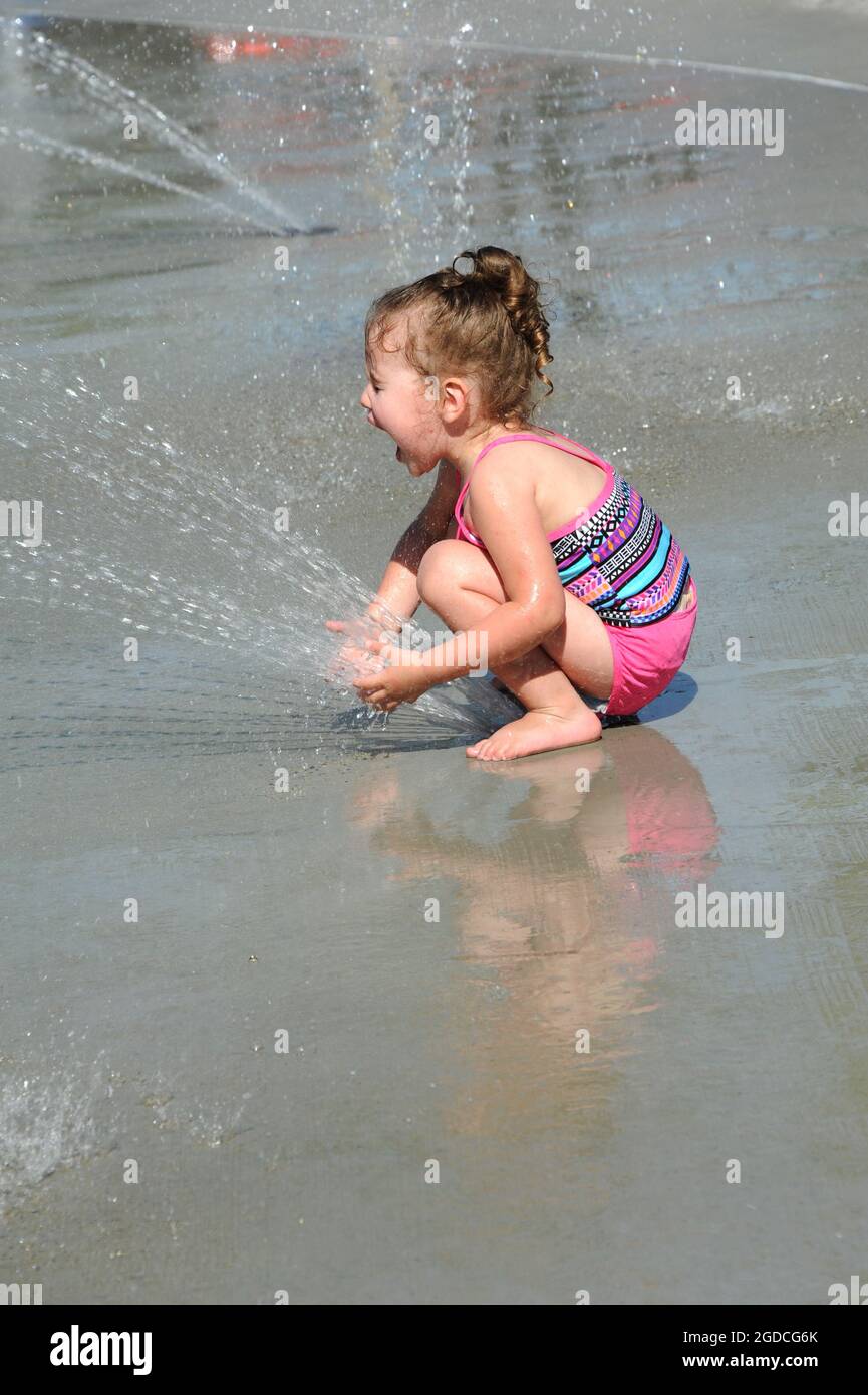 Un Bebe Qui Se Met A Genoux Par Dessus L Event De Pulverisation Du Parc Aquatique La Bouche Est Ouverte Et Les Yeux Fermes Comme Elle Exprime Son Plaisir Combinaison De Bain Rose Et