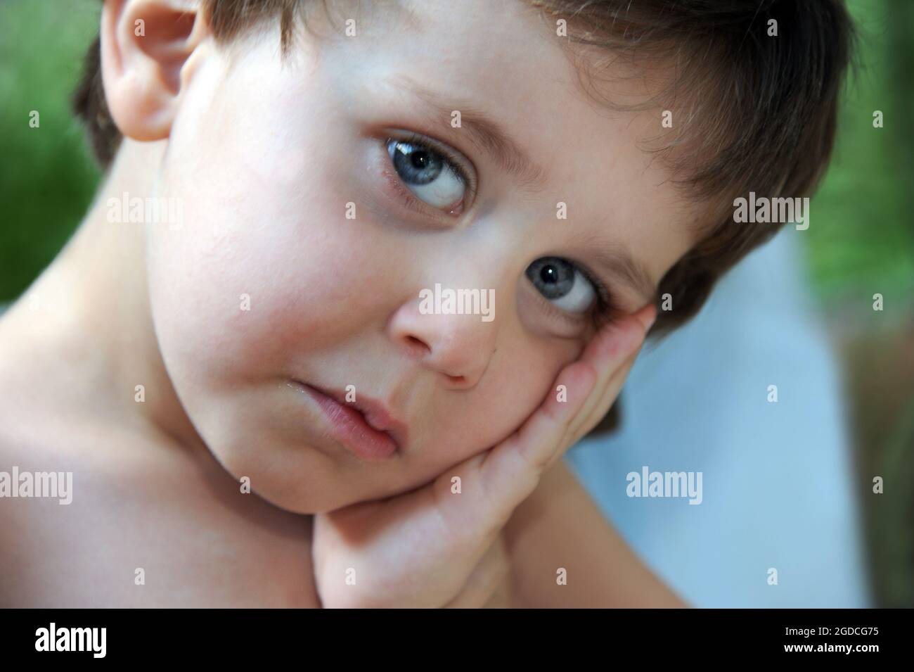 Gros plan d'un petit garçon semble très triste. Il penche la tête sur sa main et regarde la caméra. Banque D'Images