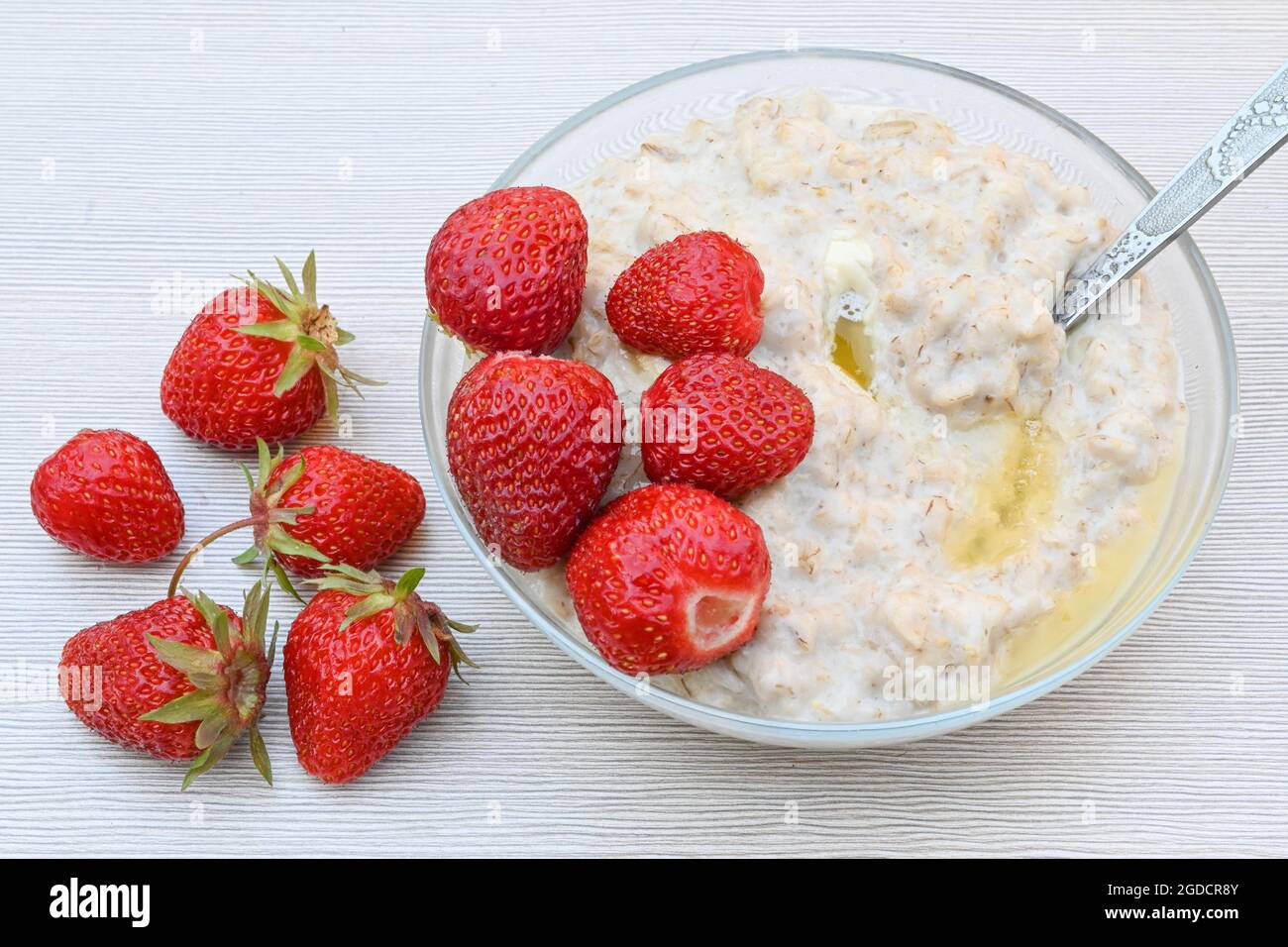 Une assiette de porridge de flocons d'avoine et de fraises juteuses mûres sur une table blanche Banque D'Images