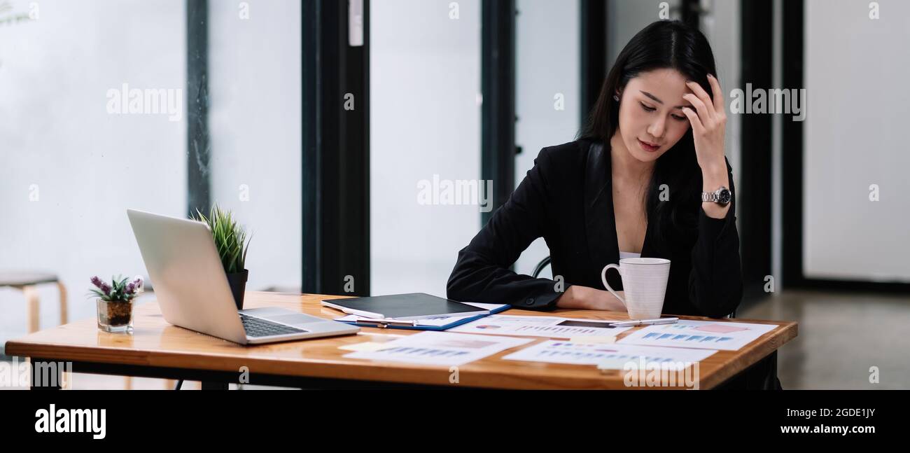 Jeune femme d'affaires asiatique assise sur le lieu de travail et travaillant avec le rapport de marketing. Famle utilisant un ordinateur portable. Banque D'Images