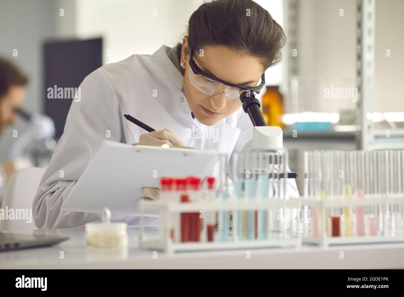 Gros plan femme scientifique travaillant en laboratoire avec un microscope et un presse-papiers Banque D'Images