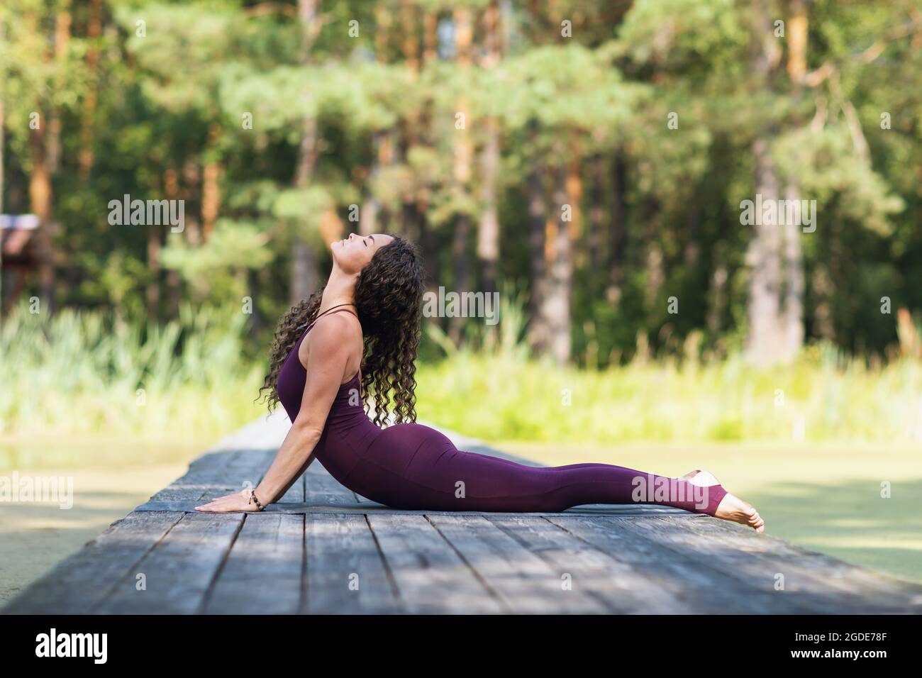 Une femme dans une salopette bordeaux pratiquant le yoga dans le parc, allongé sur un tapis, exécute l'exercice Bhujangasana, la posture Cobra Banque D'Images