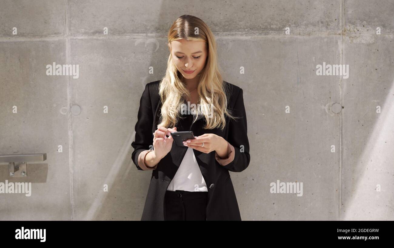 Femme d'affaires parcourant un téléphone portable près d'un mur en béton Banque D'Images