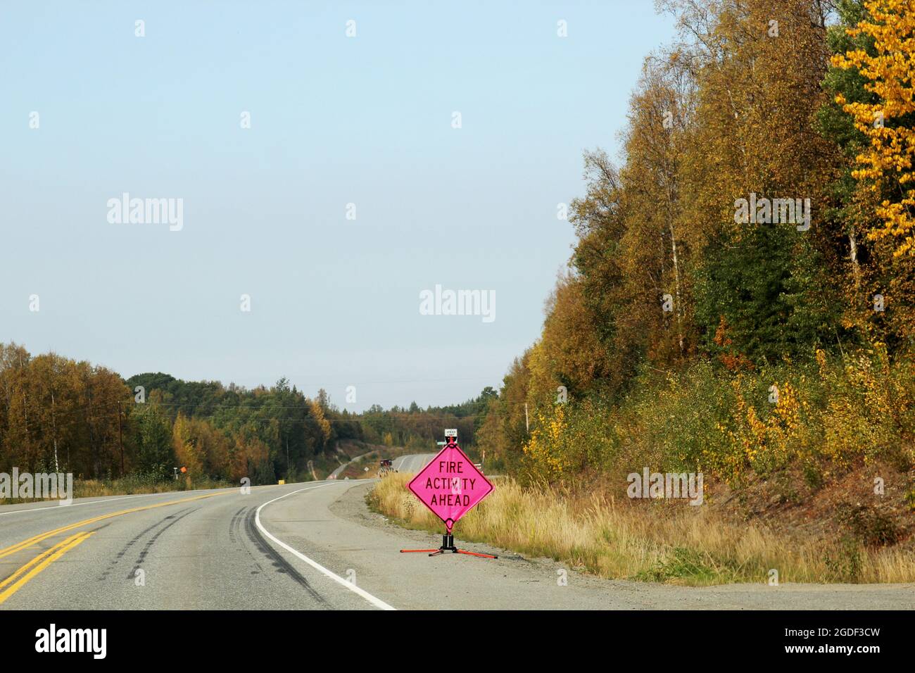 Ammerikanisches Verkehrszeichen mit der Aufschrift 'Fire acitivity Ahead' in leuchtendem Pink am Straßenrand auf einer Hauptverkehrsstraße Alaska, USA. Banque D'Images
