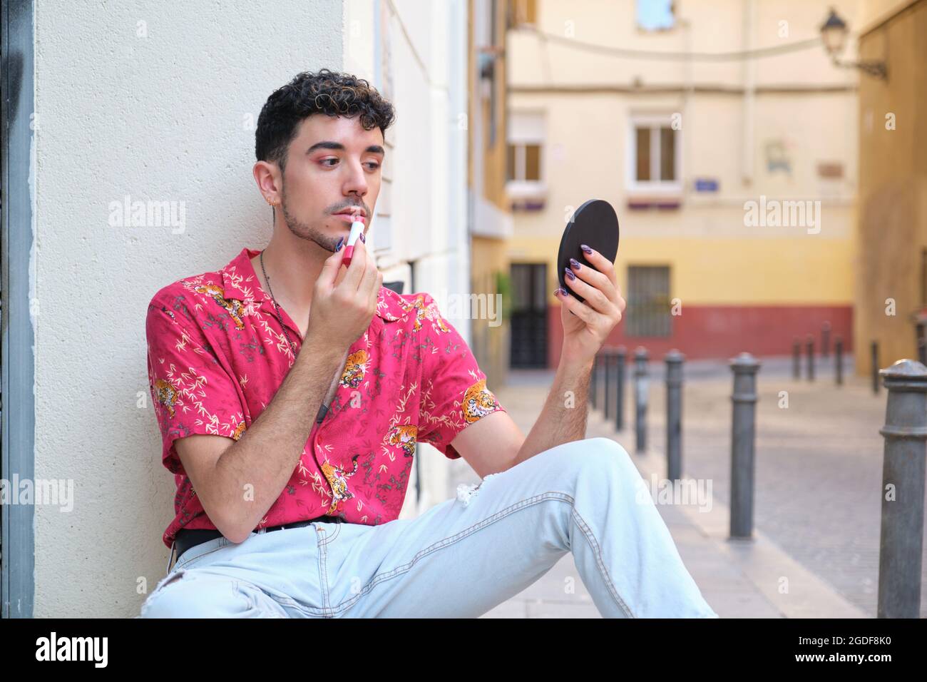 Jeune homme caucasien avec de longs ongles faux appliquant rouge à lèvres dans la rue. Banque D'Images