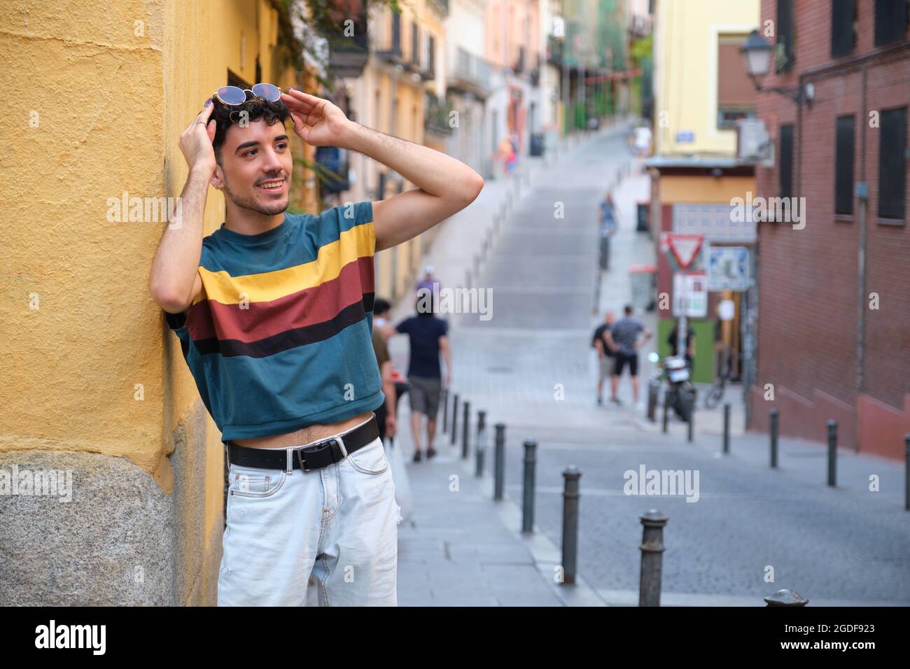 Jeune homme caucasien avec de longs ongles faux souriant et debout contre un mur. Banque D'Images