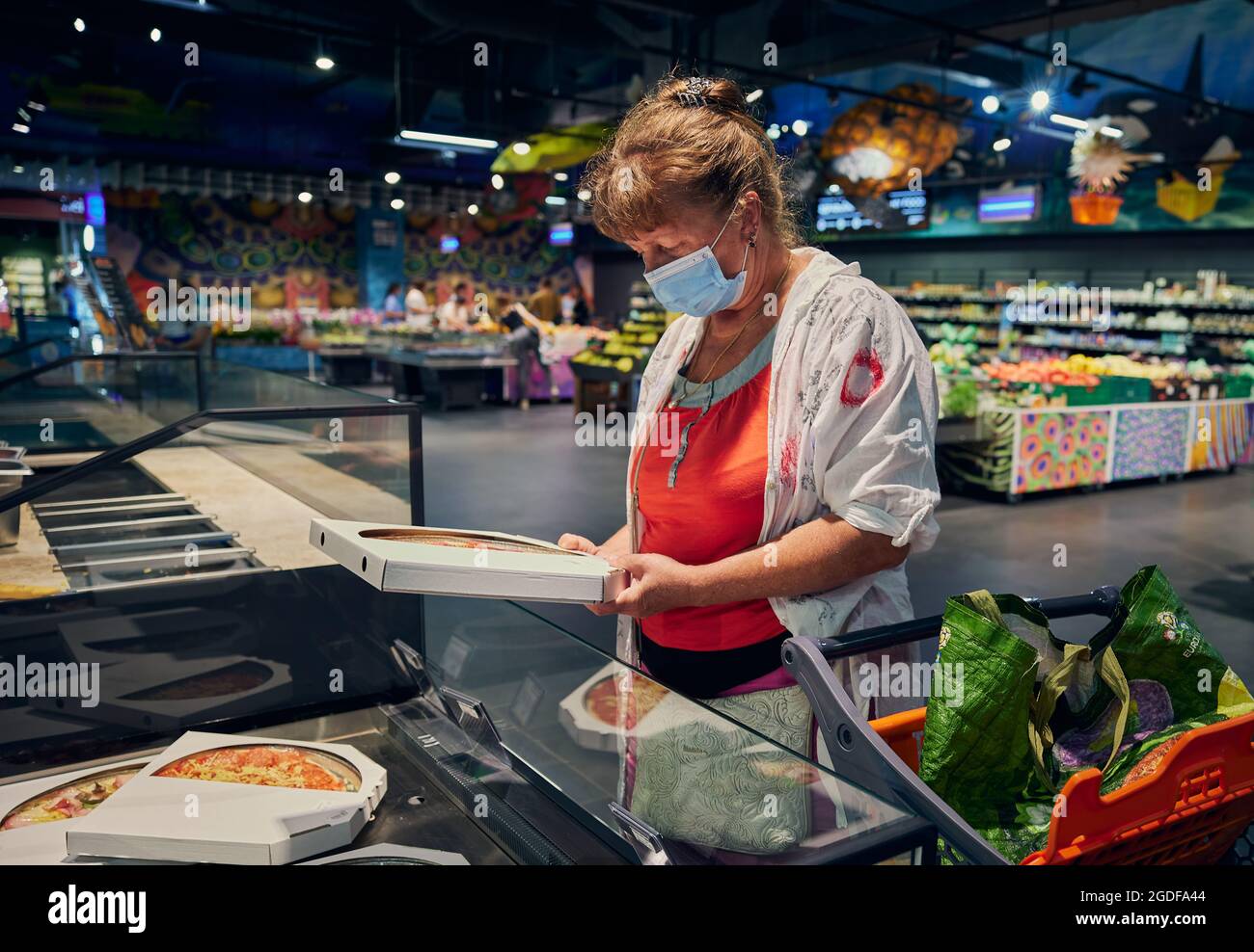 Une jolie femme âgée dans un masque médical choisit de la pizza dans une épicerie. Odessa Ukraine, magasin d'alimentation Silpo. Banque D'Images