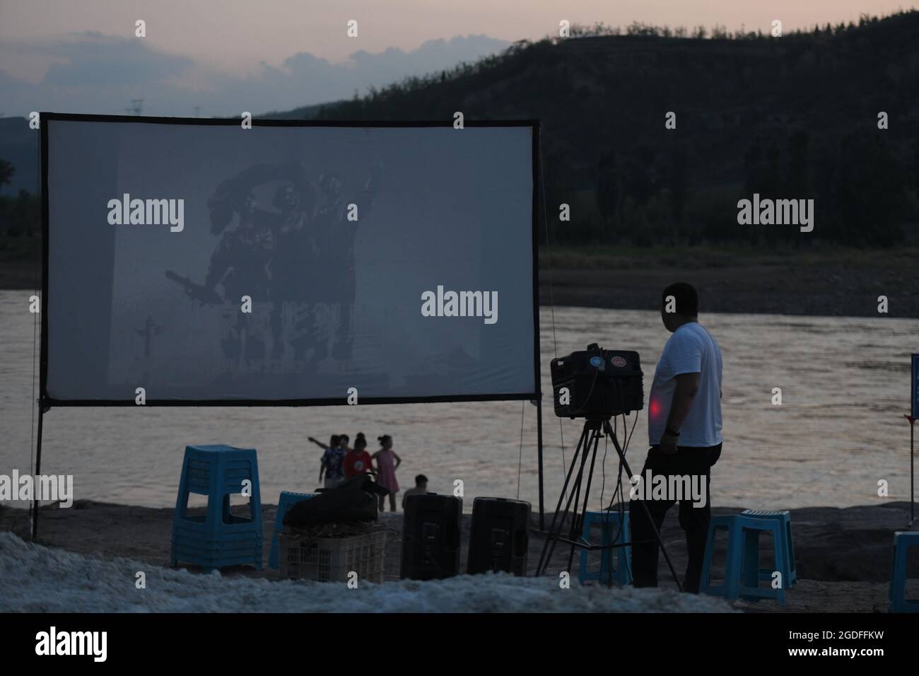 (210813) -- TAIYUAN, 13 août 2021 (Xinhua) -- Xue Xiaogang (L) ajuste les dispositifs de projection de films par la rivière Yellow, dans le canton de Sanjiao, comté de Liulin, province du Shanxi, dans le nord de la Chine, le 14 juillet 2021. En 1975, le canton de Sanjiao a créé une équipe de projection de films. Liu Bufei et Liu Dengzhao, tous deux cinéphiles depuis leur enfance, se sont joints à l'équipe et sont devenus des projectionnistes ruraux. En 2007, l'équipe est devenue une troïka alors que le projectionniste de deuxième génération Xue Xiaogang s'est joint à lui, qui avait vu des films en plein air dans le village tout en grandissant. Au fil des ans, l'équipe de projection, depuis d'innombrables fois Banque D'Images