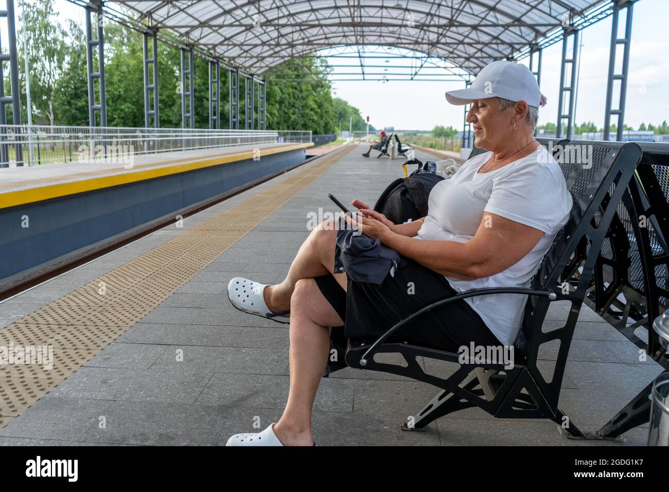 Une femme active âgée voyage. Il est situé à la gare et trace l'itinéraire dans le téléphone. Grand-mère itinérante. Plate-forme de train. Le passager est Banque D'Images