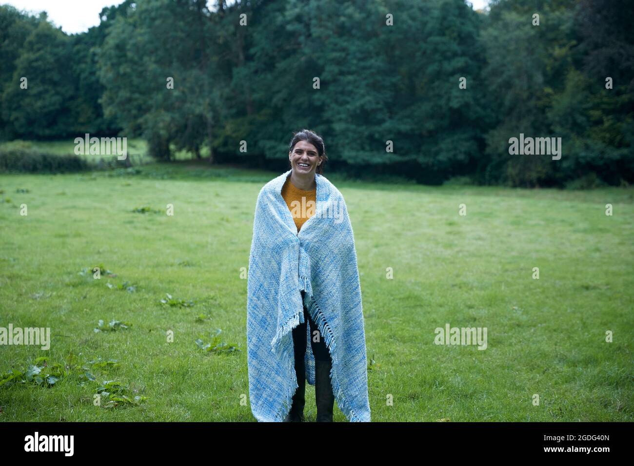 Mid adult woman standing in rural field enveloppé dans une couverture, portrait Banque D'Images