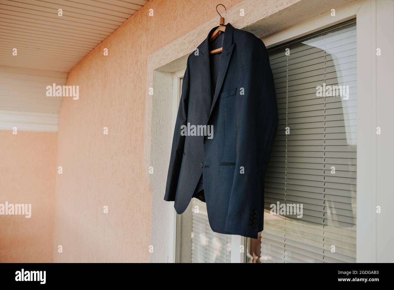 Une veste noire est suspendue contre une fenêtre blanche dans la pièce. Blazer classique classique bleu foncé brun noir pour hommes. Vêtements de mode pour hommes d'affaires Banque D'Images
