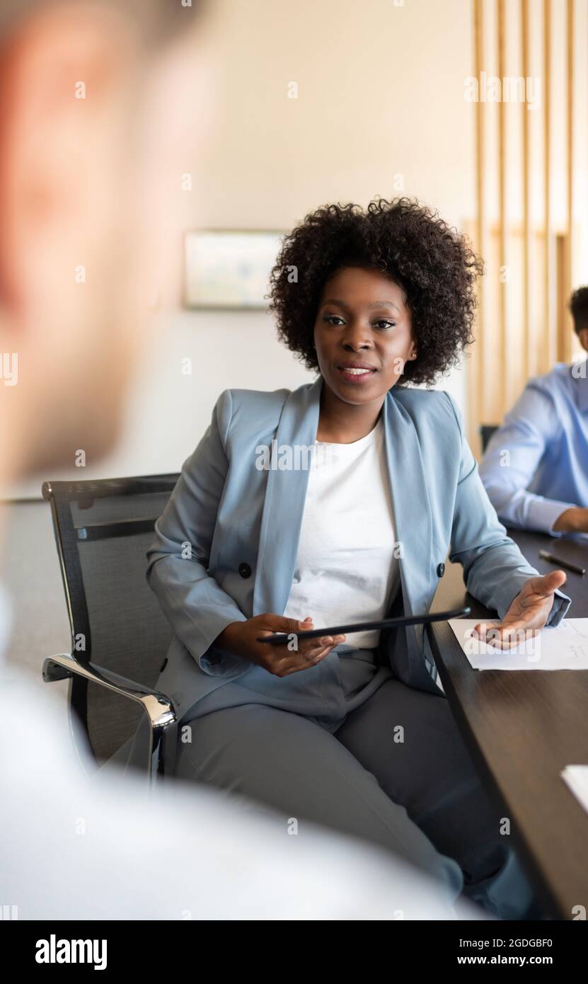 Patron afro-américain avec tablette discutant des données avec les employés pendant le séminaire Banque D'Images Patron afro-américain avec tablette discutant des données avec les employés pendant le séminaire Banque D'Images