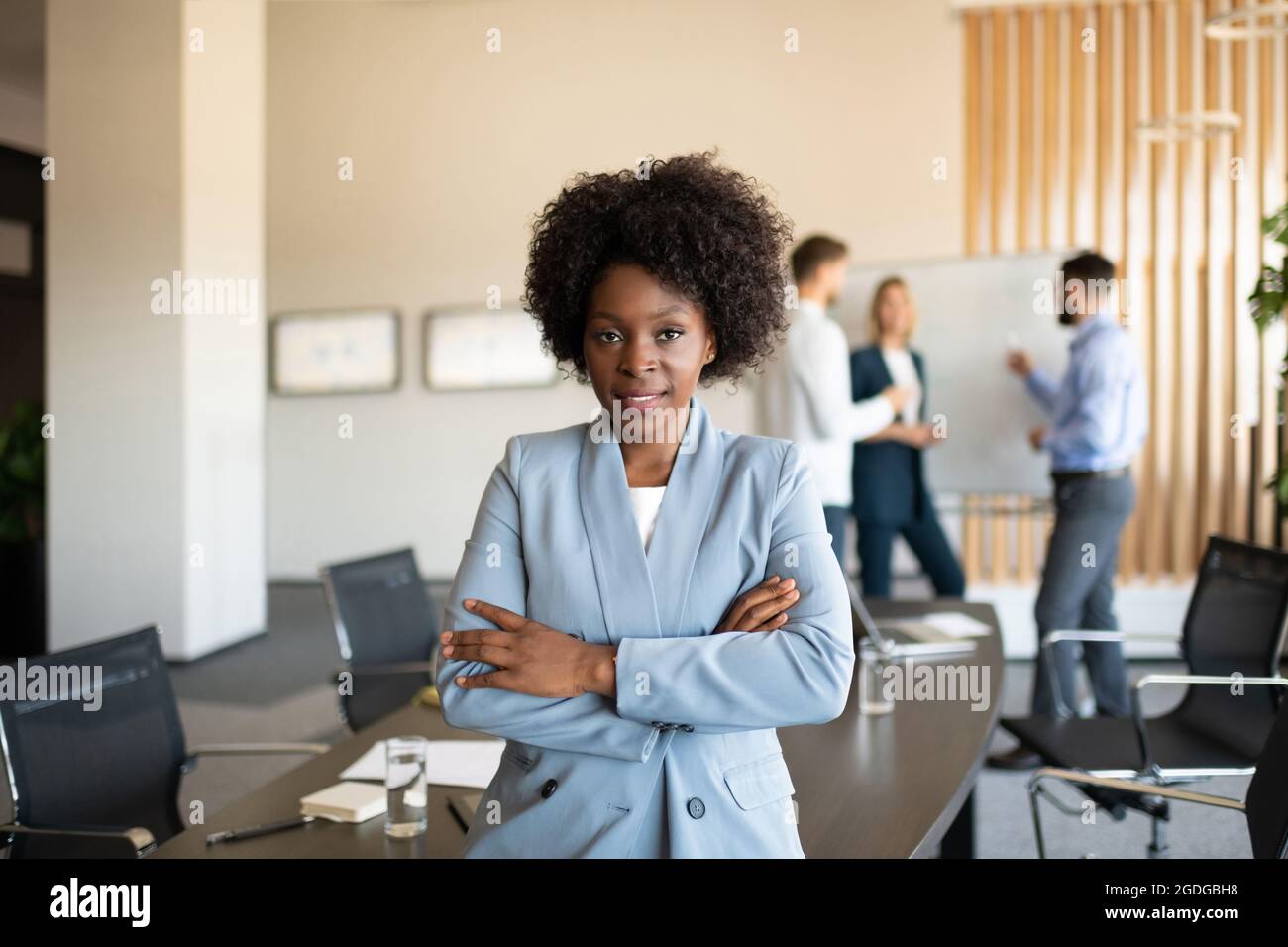 Joyeux directeur noir qui croise les bras et sourit tout en s'appuyant sur la table pendant la réunion Banque D'Images Joyeux directeur noir qui croise les bras et sourit tout en s'appuyant sur la table pendant la réunion Banque D'Images