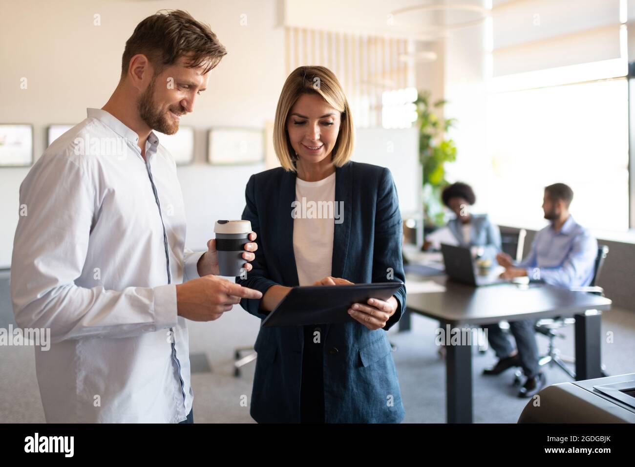 Homme et femme positifs souriant et parcourant les données sur une tablette pendant le travail au bureau Banque D'Images