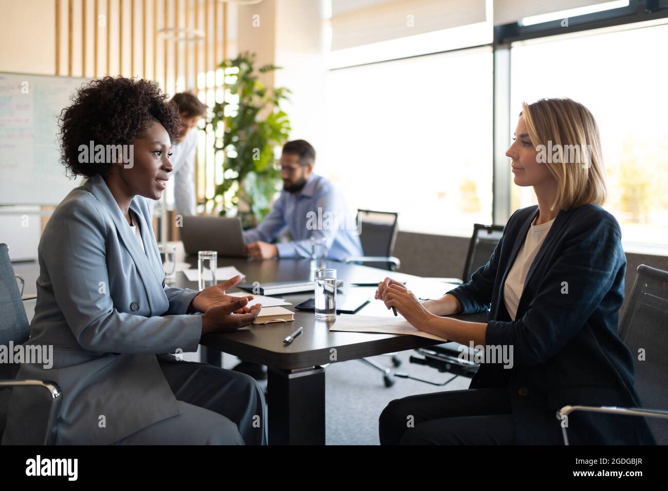 Collègues multiraciaux assis à la table et parlant pendant la réunion Banque D'Images Collègues multiraciaux assis à la table et parlant pendant la réunion Banque D'Images