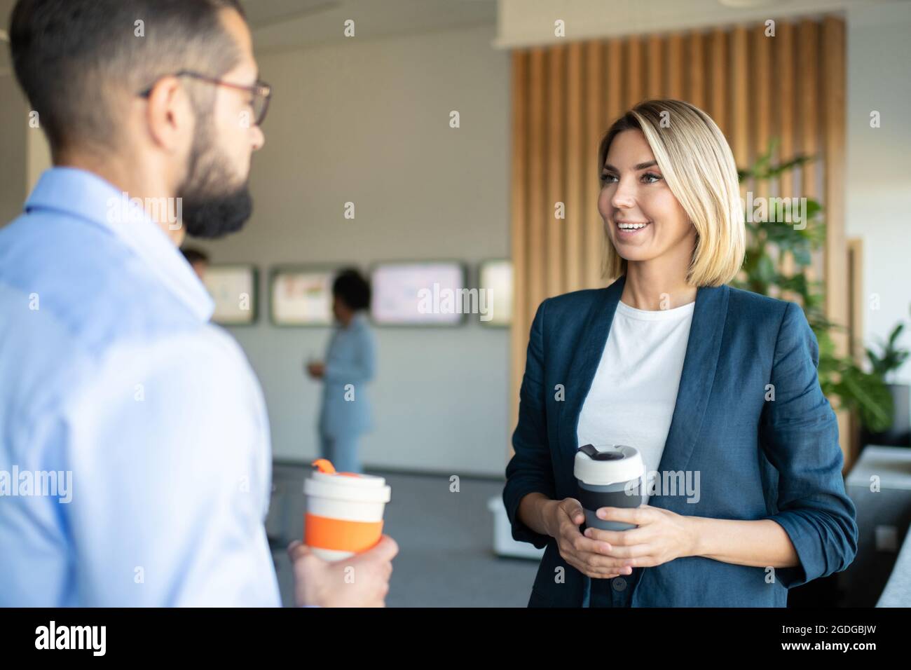 Homme et femme heureux avec des boissons pour aller sourire et bavarder pendant la pause au bureau Banque D'Images Homme et femme heureux avec des boissons pour aller sourire et bavarder pendant la pause au bureau Banque D'Images