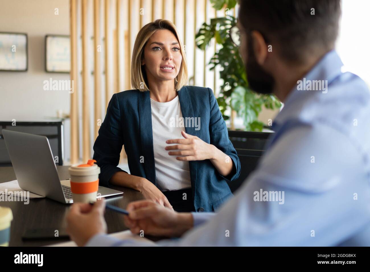 Femme gestionnaire parlant avec un collègue pendant qu'elle est assise à table pendant le travail Banque D'Images Femme gestionnaire parlant avec un collègue pendant qu'elle est assise à table pendant le travail Banque D'Images