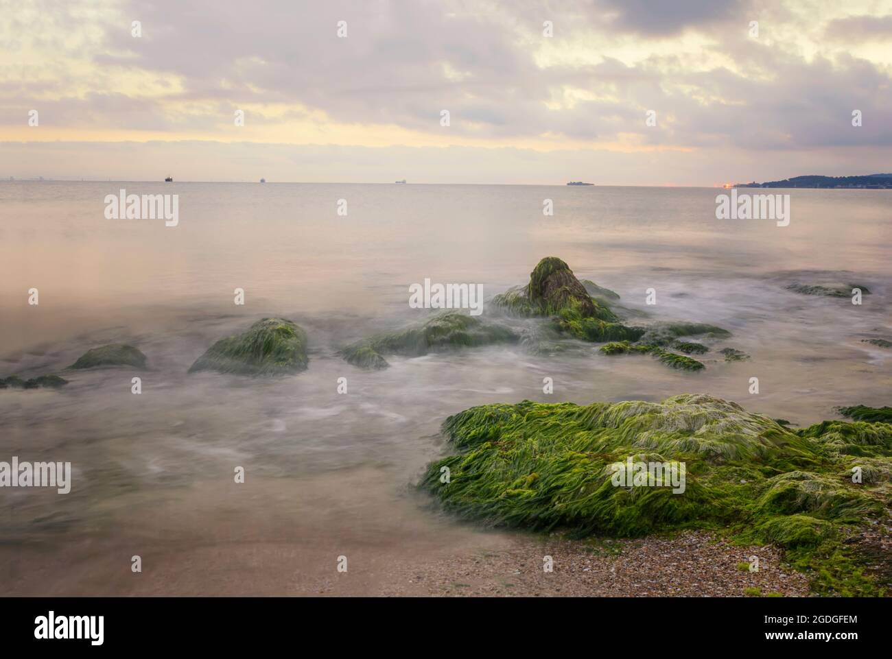 Un incroyable lever de soleil sur la mer avec un obturateur lent et des vagues qui s'écoulent autour d'une grande roche sur une plage de sable Banque D'Images