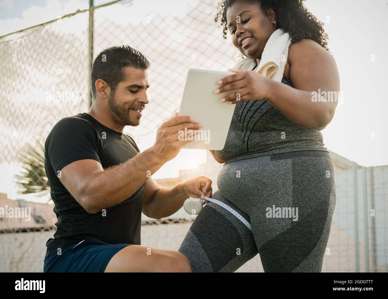 Entraîneur personnel travaillant avec une femme curvy mesurant son corps tout en lui donnant des instructions avec la tablette numérique pendant la session d'entraînement Banque D'Images