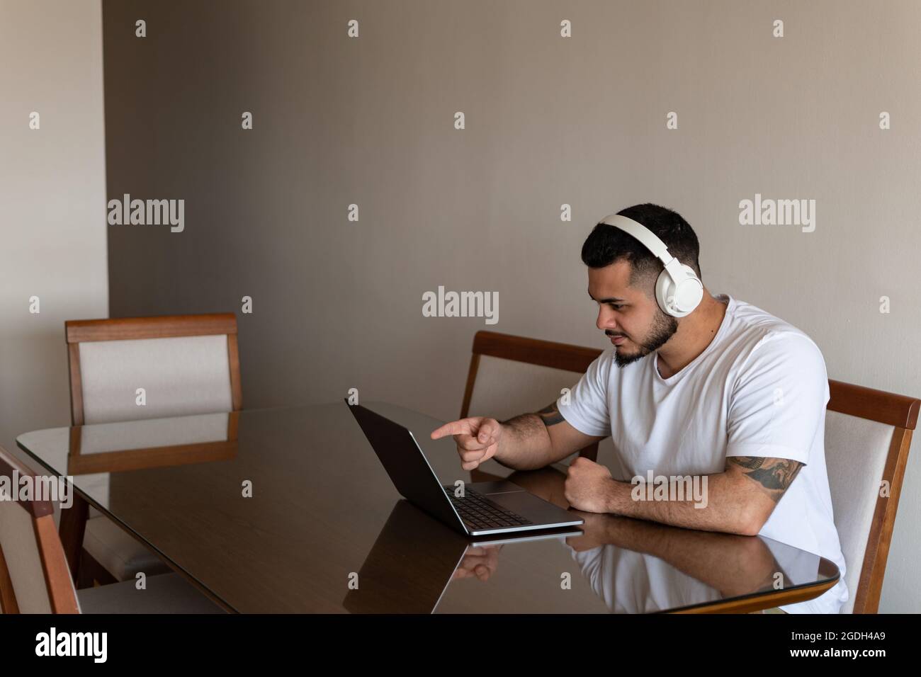 Latino homme avec des tatouages et des écouteurs pointant son doigt sur l'écran de l'ordinateur portable Banque D'Images