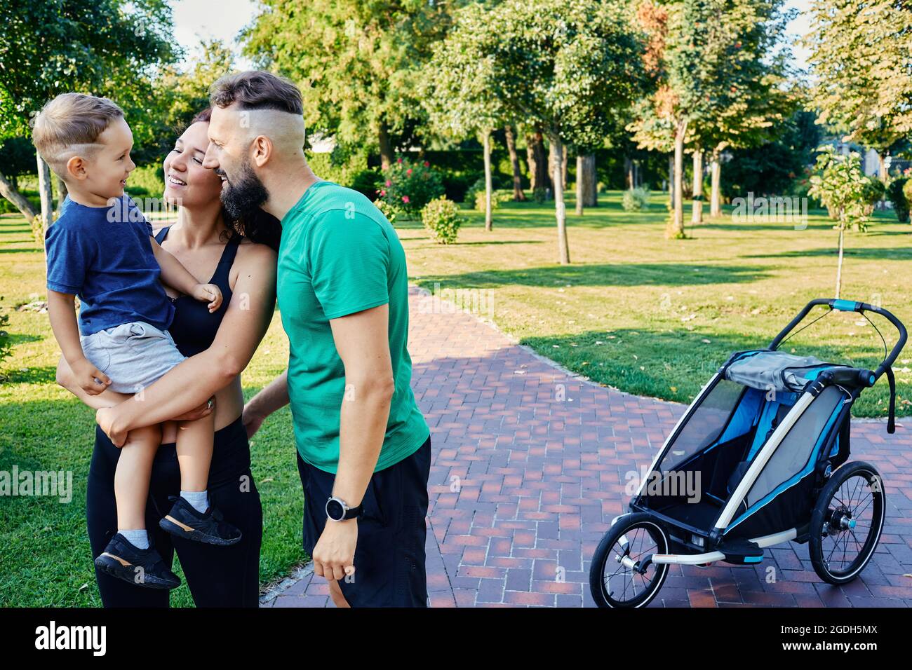 Famille active avec leur fils après un jogging matinal avec une poussette de jogging dans un magnifique parc. sports pour toute une famille Banque D'Images