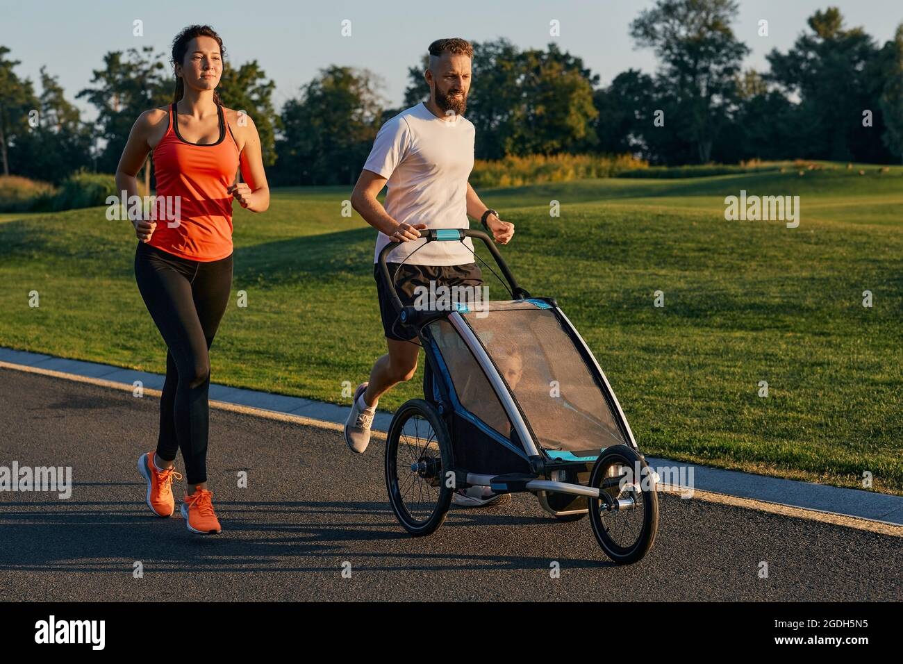 Jeune famille avec leur enfant dans une poussette de jogging pendant le jogging dans un parc. Famille active courant Banque D'Images