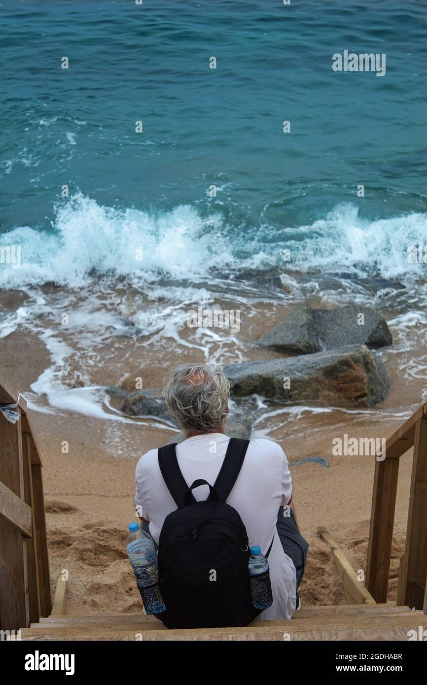 homme mature avec cheveux gris et un sac à dos assis sur une échelle en  bois au bord de la mer Photo Stock - Alamy
