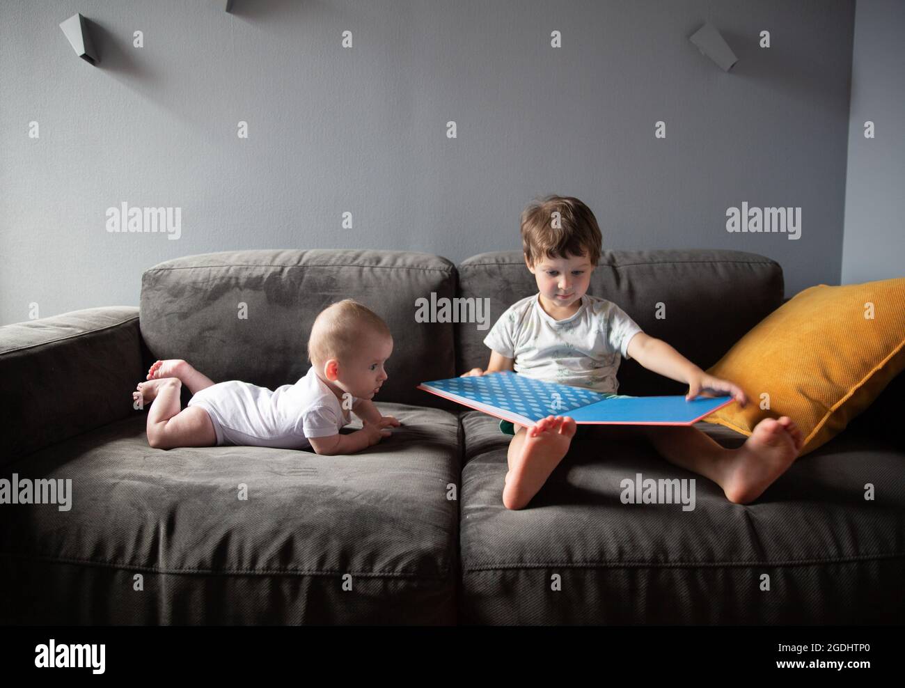 garçon lit un livre assis sur le canapé et son frère est couché à proximité Banque D'Images