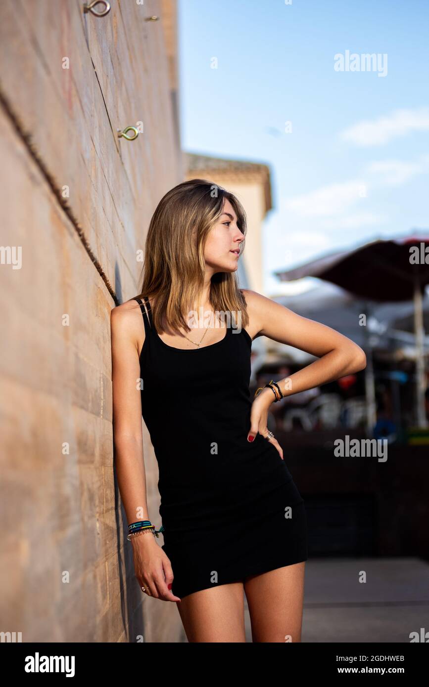 Jeune blonde blanche fille avec une robe noire appuyé contre un mur dans un  cadre uban Photo Stock - Alamy
