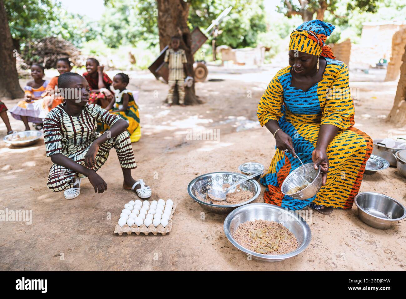 Souriante, femme africaine noire assise sur un petit chiar, divisant le repas de sa famille, son fils s'agenouillant à côté d'elle en attendant son bol Banque D'Images